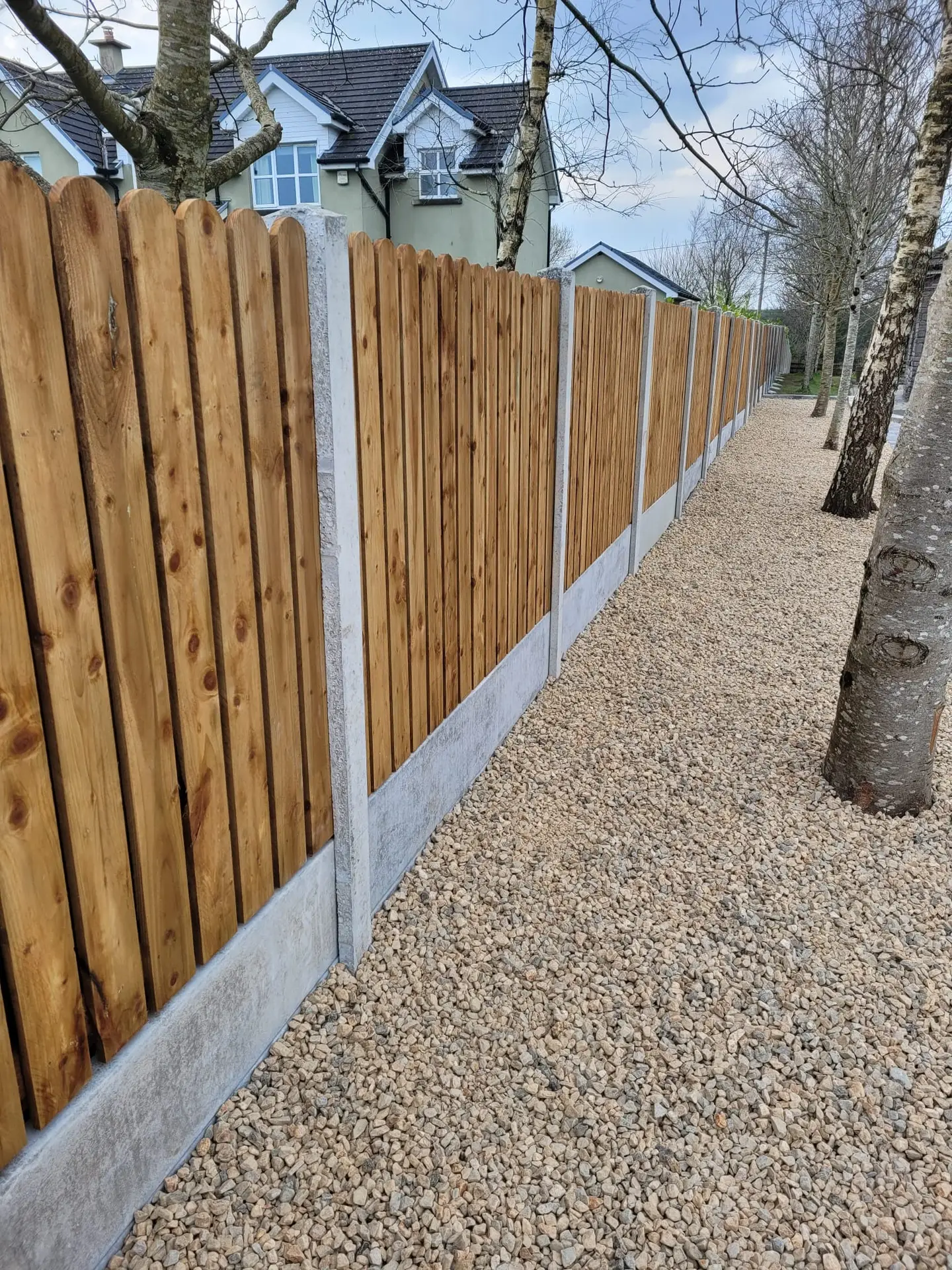 Concrete post and timber panel fencing installed over decorative gravel